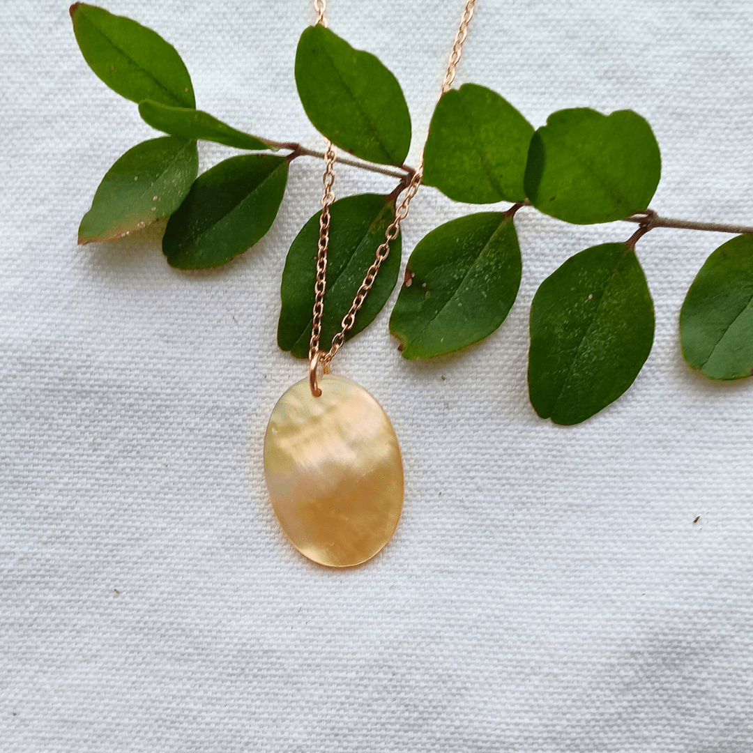 Gold necklace with oval pendant on greenery.