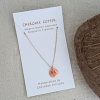 Copper necklace with turtle pendant on white card.