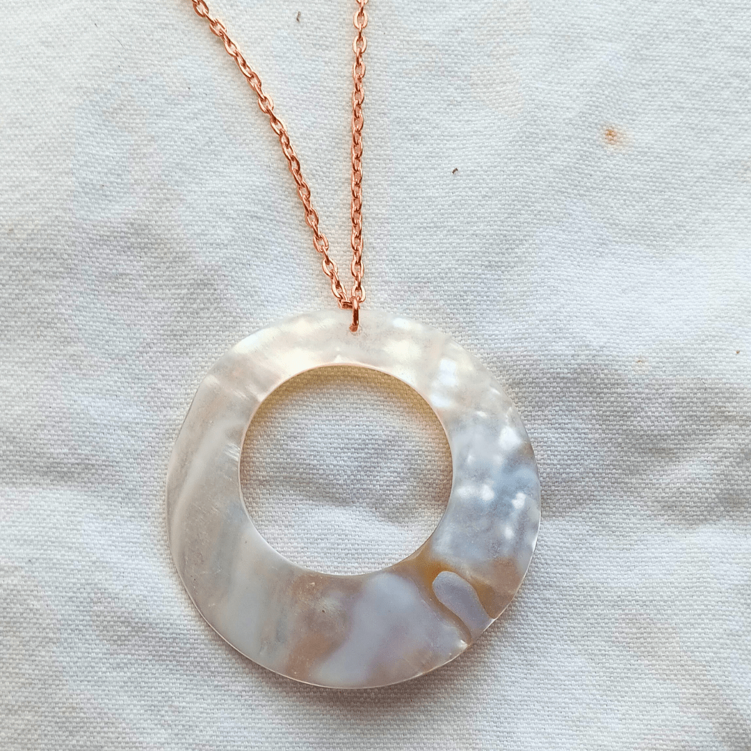 Circular mother-of-pearl pendant necklace on white fabric.